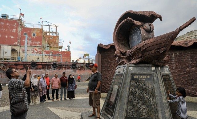 Pengunjung berfoto di tugu dalam kompleks Kapal PLTD Apung yang memuat nama-nama warga setempat yang meninggal saat Tsunami Aceh. Foto: Suparta/acehkini